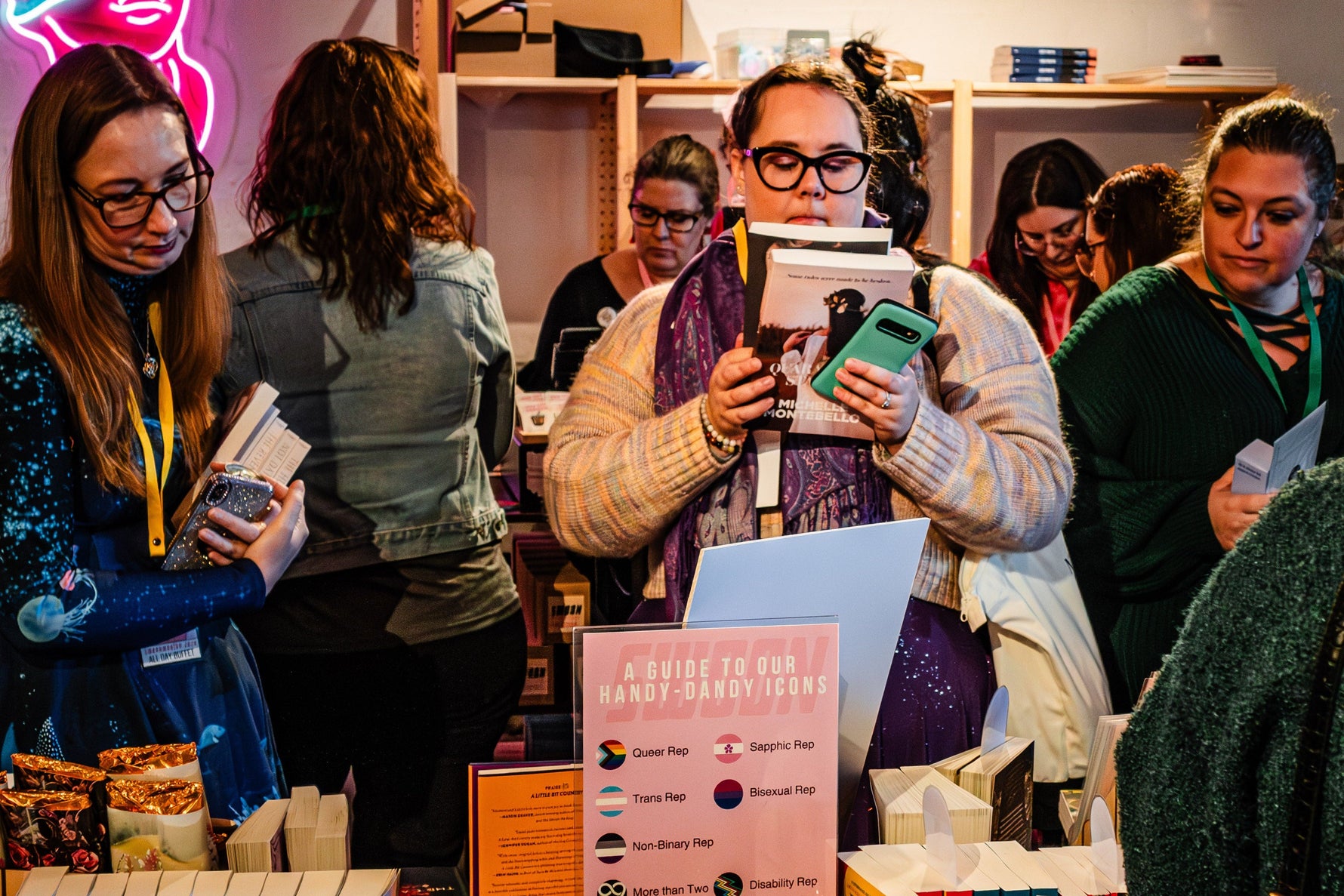 People browsing books at a book fair with a neon sign in the background